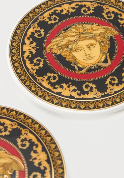 Δύο διακοσμητικά πιάτα με χρυσό και μαύρο περίπλοκο περιθώριο και κεντρικό σχέδιο με κεφάλι Μέδουσας σε κόκκινο φόντο.