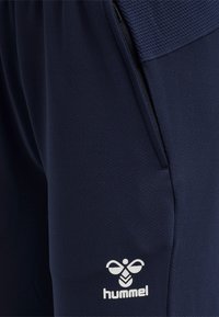 Marineblauwe, getextureerde sportbroek met ritszak en wit hummel-logo op het bovenbeen.
