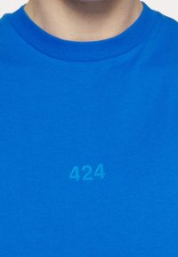 Modrá bavlněná tričko s kulatým výstřihem, na přední části ve středu je tištěné číslo "424" v jemném odstínu. Hladká textura.
