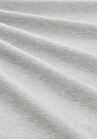 Tela de algodón gris claro con una textura suave, que presenta sutiles ondulaciones y una superficie lisa, mostrando un patrón de color uniforme.