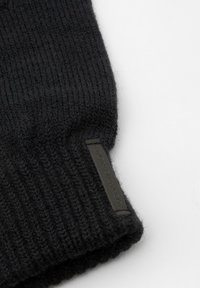 Căciulă tricotată neagră cu textură ribatată. Prezintă un eticheta rectangulară neagră cu text în relief pe margine.