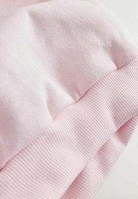 Tissu de sweat-shirt rose clair avec une texture douce. Présente un poignet côtelé à l'ourlet pour un ajustement confortable. Les détails des coutures sont visibles.