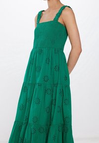 Grön bomullsklänning med fyrkantig halsringning, smockad byst, volangiga axelband och fyrkantad kjol med broderade blommönster.