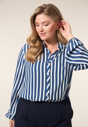 Gestreepte blouse in blauw en witte stof, met lange mouwen en elastische manchetten, in een relaxte pasvorm, gecombineerd met donkere broek.
