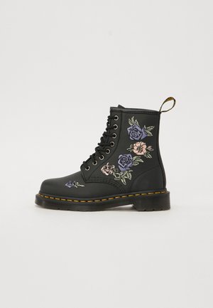 Bottine en cuir noir avec broderie florale en violet et rose. Comprend des lacets noirs, des coutures jaunes et une languette.