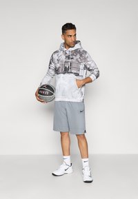 Grå hættetrøje med grafisk design, sammen med grå atletiske shorts. Hvide sneakers og en basketball fuldender outfittet.