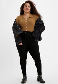 Top de manga larga acanalado en color camel con botones, combinado con unos vaqueros negros de cintura alta y una chaqueta de mezclilla negra de gran tamaño. Botas negras de tacón.