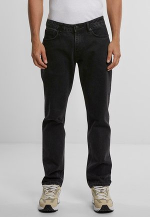 Schwarze Denim-Jeans mit geradem Schnitt, Fünf-Taschen-Design und klassischem Knopfverschluss, kombiniert mit hellen Sneakers.