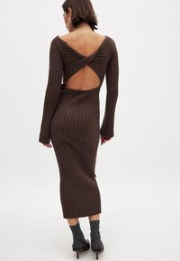 Robe en tricot côtelé marron avec manches longues, décolleté en V au dos et silhouette cintrée. Présente un tissu texturé et un design longueur cheville.