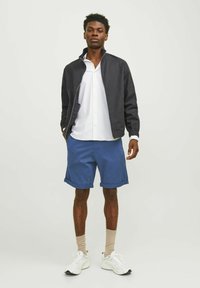 Veste navy légère, chemise blanche à rayures avec boutons, shorts bleus, chaussettes beiges et baskets blanches. Texture lisse avec un design décontracté.