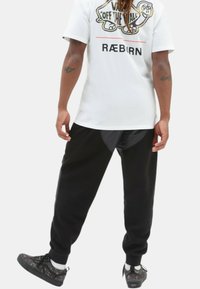Hvid t-shirt med grafisk print på ryggen, parret med sorte joggers med elastisk talje og grå paneldetalje, båret med mønstrede sneakers.