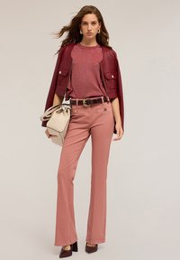 Chaqueta de imitación cuero burdeos, blusa brillante rosa, pantalones de campana rosa claro, cinturón marrón con herrajes dorados, bolso blanco y tacones burdeos.