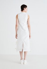 White sleeveless dress with a straight cut, featuring a back slit and ribbon accents on the sides, made from a smooth fabric.