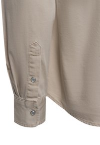 Beige long-sleeve shirt with a textured fabric, featuring a buttoned cuff and pleated detail at the sleeve for added design.
