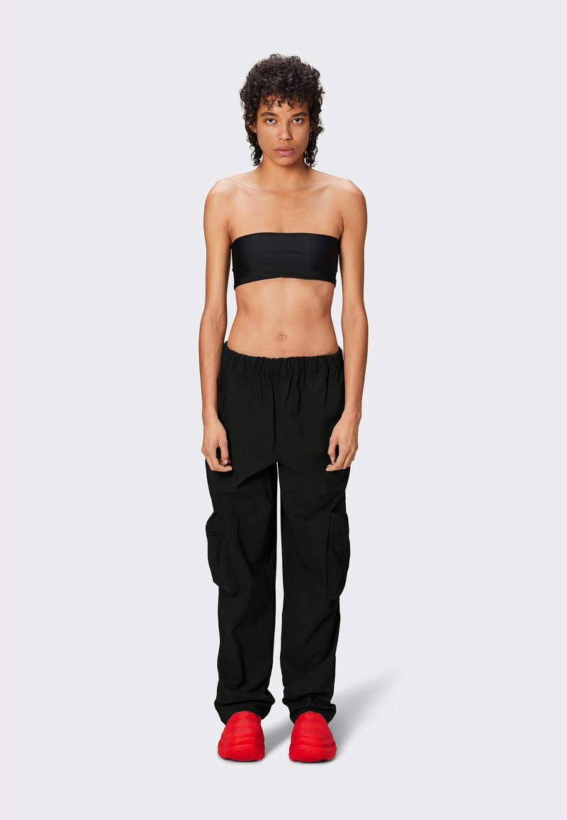 Top bandeau nero corto, pantaloni cargo neri rilassati con tasche e scarpe rosse; sfondo semplice, modello in piedi di fronte.