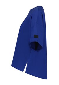 T-shirt bleu à manches courtes avec un col rond, fentes latérales et une petite étiquette noire sur la manche. Texture de tissu lisse.