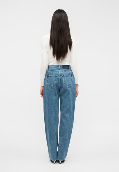 Χαλαρά μπλε τζιν με ψηλή μέση. Διαθέτουν δύο πίσω τσέπες και λεπτομέρειες διακριτικής ραφής. Φοριούνται με λευκό τοπ.