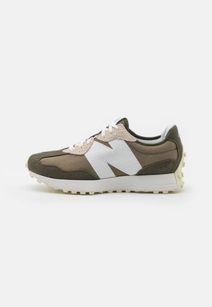 Sideligt billede af en brun og beige sneaker med en stor hvid "N" logo og hvid sål på en ensfarvet hvid baggrund.