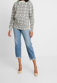 Mikina s kapucí s černobílým motivem hadí kůže, doplněná světle modrými krátkými džínami s roztřepenými lemy a béžovými špičatými lodičkami.