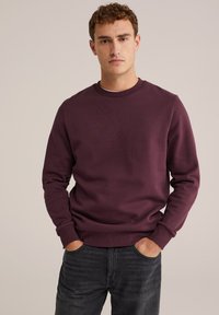 Felpa bordeaux con collo a giro, maniche lunghe e polsini e orlo a coste. Texture liscia, abbinata a jeans neri.