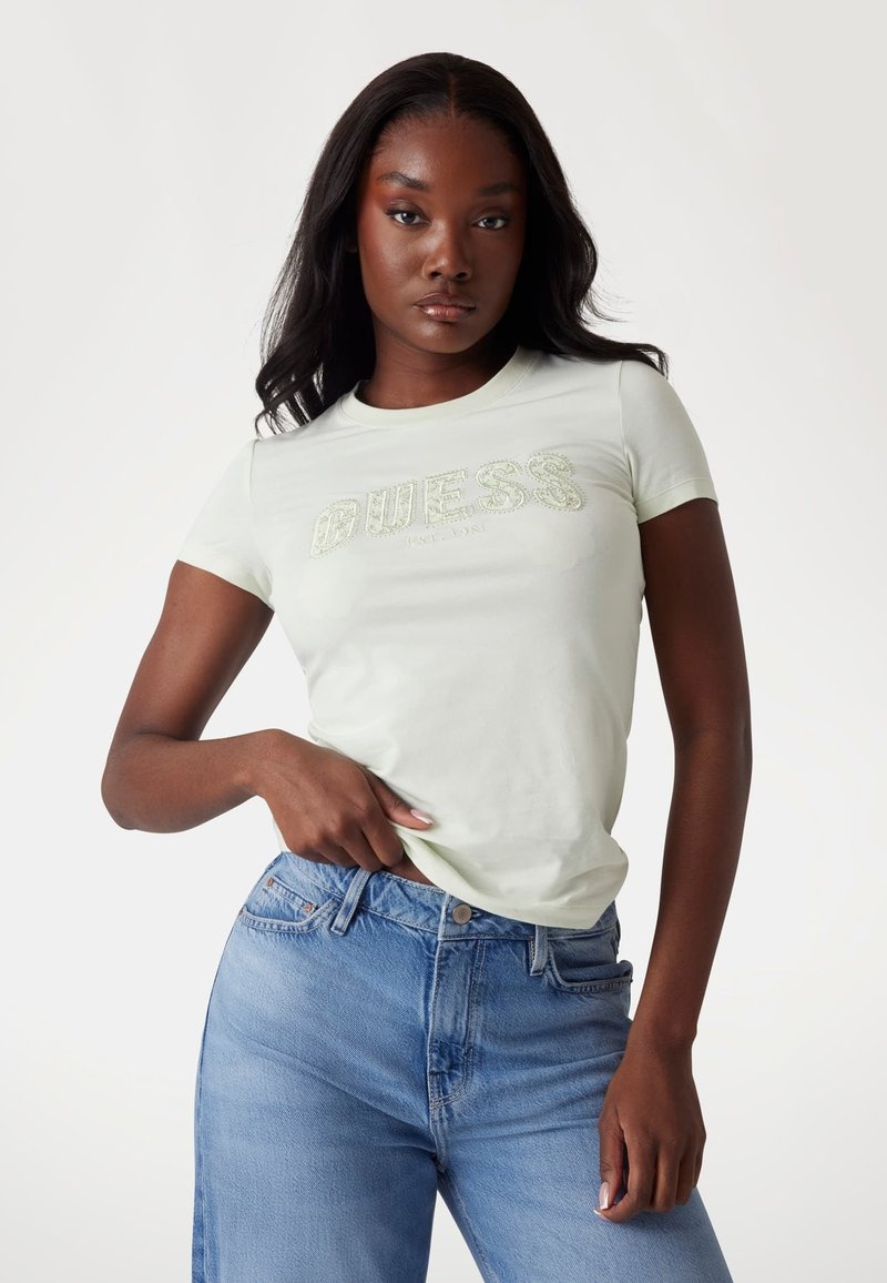 Lys grøn fitted t-shirt med korte ærmer, der har et struktureret "GUESS" logo. Sat sammen med højttaljede blå denim jeans.