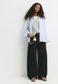 Ljusblå randig oversized skjorta, grå t-shirt, högmidjade svarta vida jeans, beige träskor med dekorationer och en charmnyckelring.