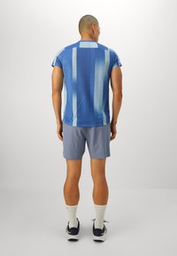 T-shirt de sport bleu avec des rayures verticales en bleu clair, associé à un short gris. Il présente des manches courtes et un col rond.
