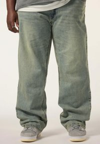 Ljusblå vida jeans med en blekt look, tillverkade av denim, med en avslappnad passform och något uppvikta fållar. Bärs med grå sneakers.