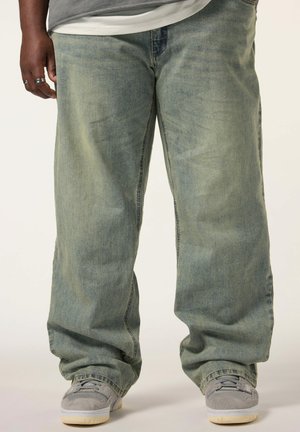 Jeans de pierna ancha de color azul claro con un aspecto desgastado, hechos de denim, con un corte relajado y dobladillos ligeramente doblados. Llevados con zapatillas grises.