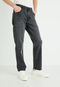 Vaqueros de mezclilla gris con corte recto, que cuentan con un diseño clásico de cinco bolsillos y una textura ligeramente deslavada. Llevados con zapatos deportivos blancos.
