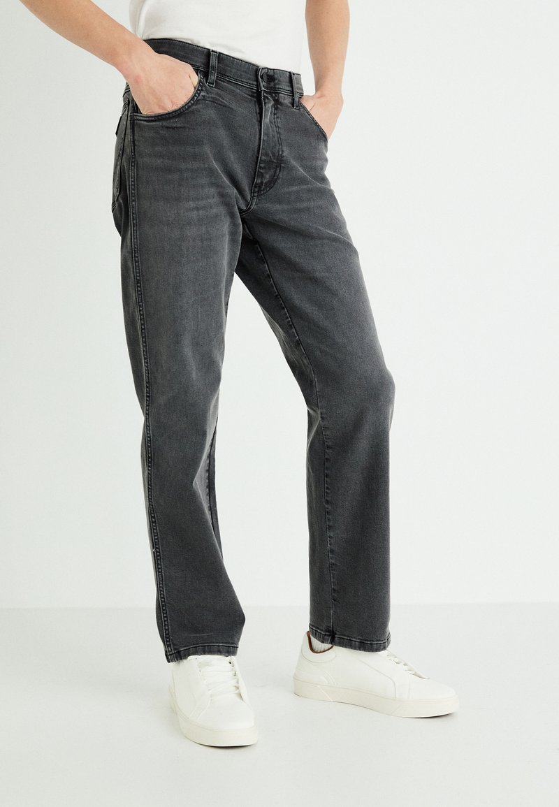 Vaqueros de mezclilla gris con corte recto, que cuentan con un diseño clásico de cinco bolsillos y una textura ligeramente deslavada. Llevados con zapatos deportivos blancos.