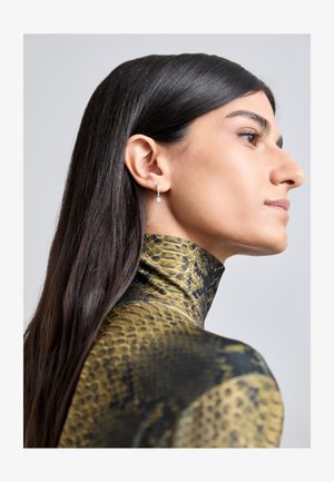 Orecchini a goccia in argento con un piccolo accento di diamante esposti su un modello che indossa una maglia a collo alto con stampa piton verde e nera.