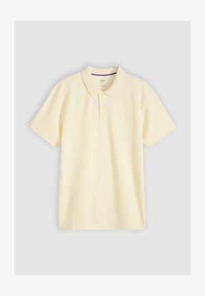 Lichtgeel polo-shirt met korte mouwen, kraag en twee knopen, weergegeven op een lichtgrijze achtergrond.