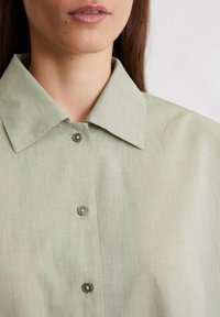 Light green collared shirt with a soft texture, featuring two buttons at the placket and a relaxed fit. Minimalistic design detail.
