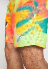 Multicolored mesh shorts featuring a tie-dye pattern in neon orange, green, and blue with a white "Jumpman" logo on the hem.