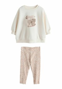 Krem pulover z zajčjim motivom in rožnatim lokom, kombiniran z svetlimi pajkicami z vseobsegajočim cvetličnim potiskom.