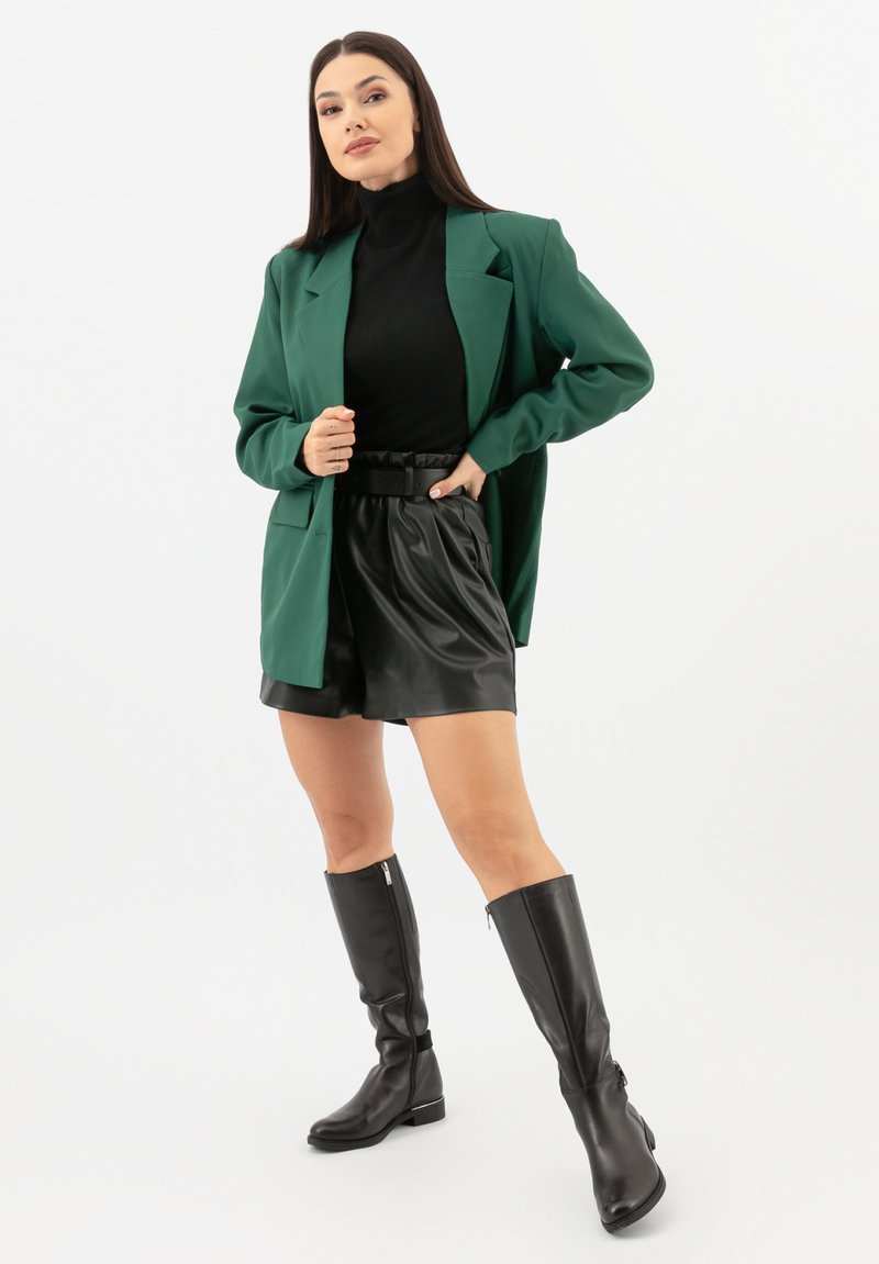 Blazer verde, dolcevita nero, pantaloncini in pelle nera e stivali neri al ginocchio. Caratterizzato da linee eleganti e una vestibilità comoda.