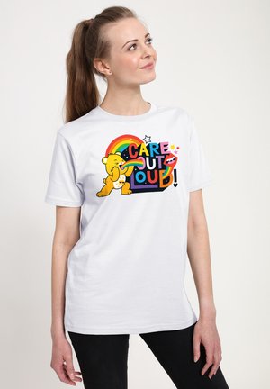 Hvid bomulds T-shirt med farverig grafikdesign med en bjørn, teksten "CARE OUT LOUD," regnbue og stjerner i livlige farver.