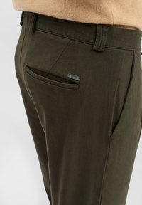 Olijfgroene broek met een gladde textuur, voorzien van een achterzak en een klein zilveren merkteken, vastgemaakt met een nette tailleband.