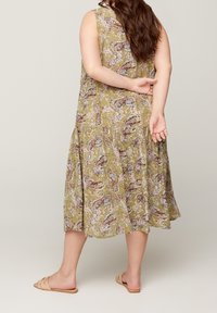 Vestido verde sin mangas con estampado floral y falda acampanada. Tela ligera con diseño de paisley; combinado con sandalias beige.
