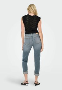 Haut sans manches en tricot noir avec un design ajouré, associé à un jean droit à revers bleu clair et des sandales à talons noirs.