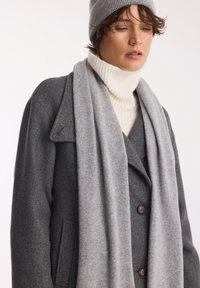 Szary wełniany płaszcz o podwójnym zapięciu i czarnych guzikach, w zestawie z kremowym, prążkowanym golfem i jasnoszarym szalikiem.