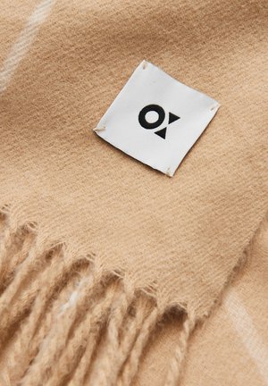Beige wool blend scarf featuring frayed edges and a small white label with a black logo. Soft texture with a plain design.