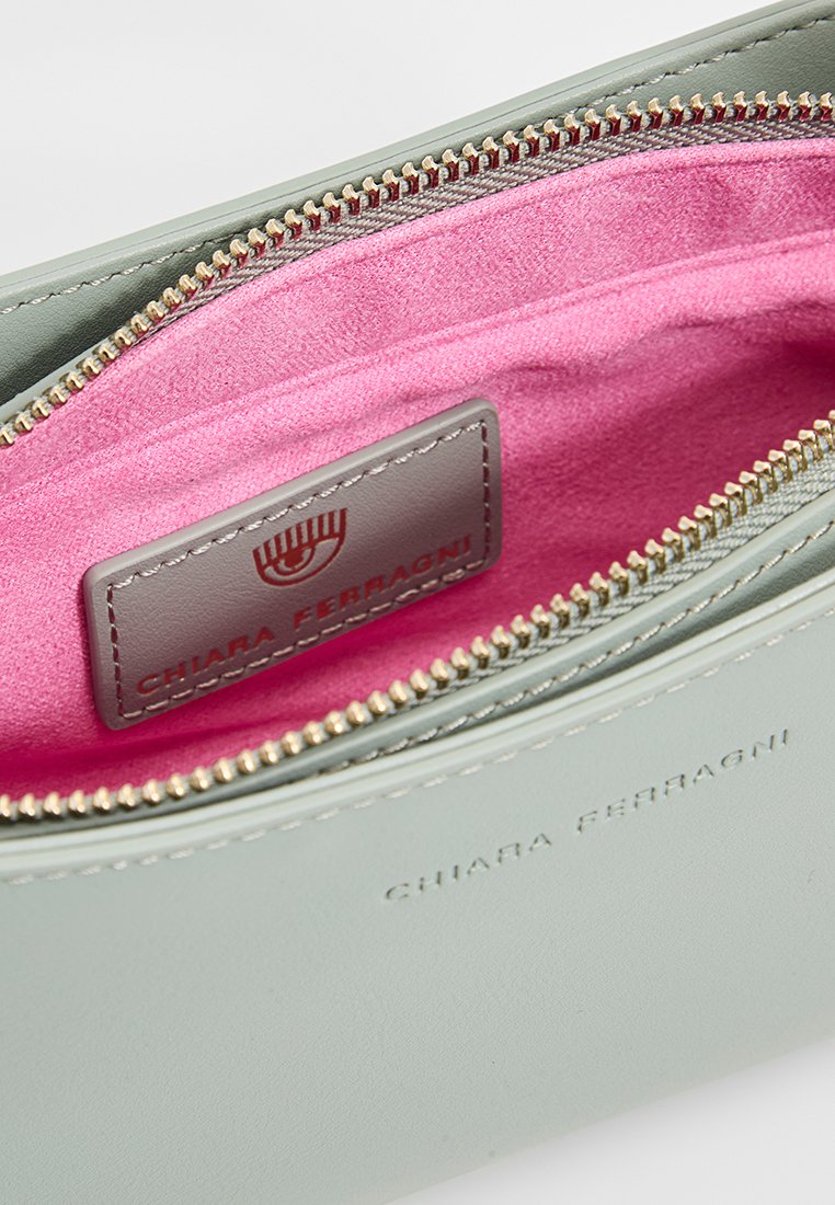 Helles grünes Lederetui mit einem pinken Innenfutter, goldener Reißverschluss und geprägtem Branding auf der Außenseite. Kompaktes und strukturiertes Design.