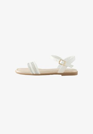 Hvid flad sandal med tre perlebesatte remme, krydsede ankelremme og en beige sål. Har et lille guldbeslag på remmen.