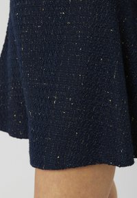 Jupe texturée bleu marine en tissu tricoté avec des éclats dorés. L'ourlet est légèrement évasé, mettant en valeur une finition lisse.