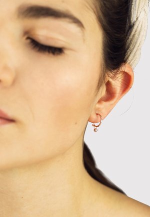 Rose gold hoop earrings with a small dangling bead. The design features smooth, rounded edges and a polished finish.