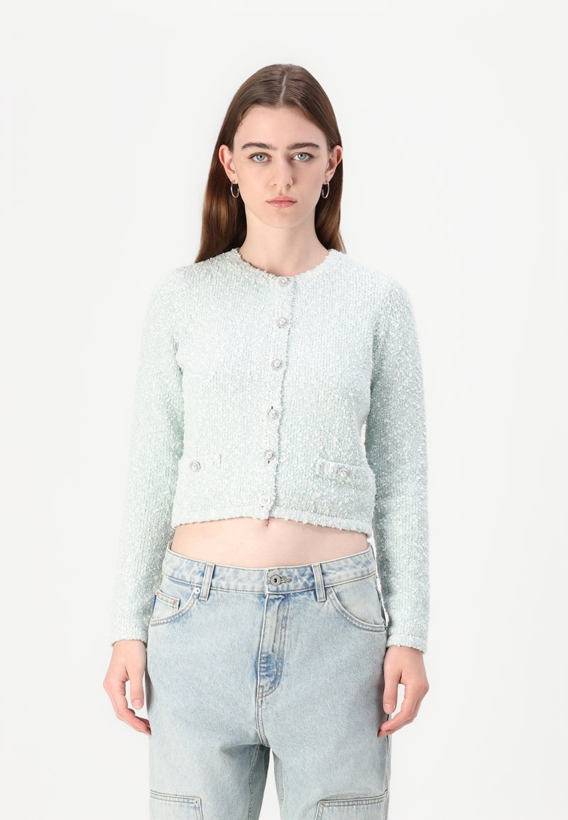 Light mint green cropped cardigan with a textured finish, round neckline, button front, and two front pockets. Paired with high-waisted jeans.