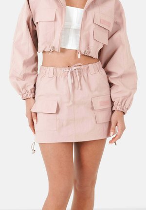 Giacca cropped di un rosa chiaro con polsini elastici e due tasche frontali, abbinata a una gonna coordinata con vita elastica e due tasche laterali.