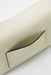 Textured light beige leather bag with a smooth finish, featuring a black-trimmed pocket on the side for added detail.